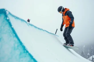 Snowboarder évaluant un kicker de freestyle au pied d'une rampe de big air dans une station alpine